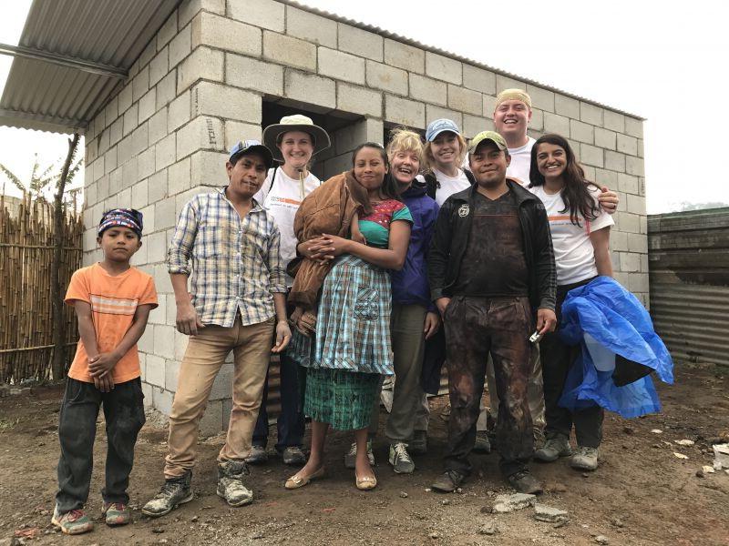 Students stand alongside the family that will live in the home they help build.